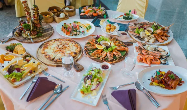 Picture of dinner table set with variety food, seafood, sushi, sashimi, pizza, barbeque, cheese and salad