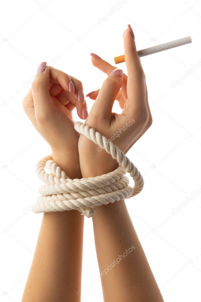 Tied female hands hold a cigarette isolated on white background.