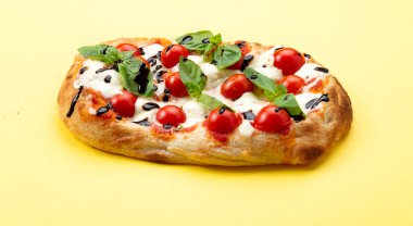 Domatesli, peynirli ve otlu Roma pizzası. Sarı arka planda.