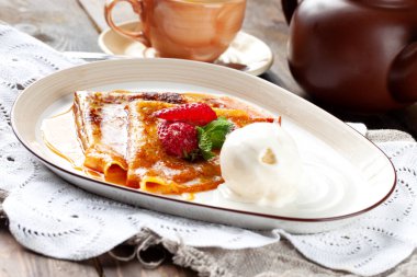 Şurupla doldurulmuş krepler, çilekle süslenmiş ve bir kepçe dondurmayla birlikte. Seçici odak.