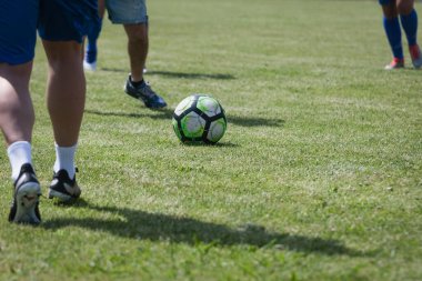 Bir futbol topu ve oyuncuların bacakları bir futbol maçında çimlerin üzerinde.