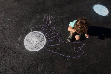 Bir çocuk yayanın asfaltına resim çiziyor.