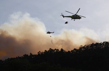 Orman yangınında uçan iki itfaiye helikopterinin silüeti.