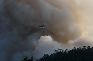 Bir helikopter orman yangınından çıkan duman bulutlarının arasında su boşaltarak uçar.