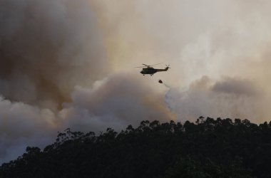 Bir helikopter orman yangınından çıkan duman bulutlarının arasında su boşaltarak uçar.