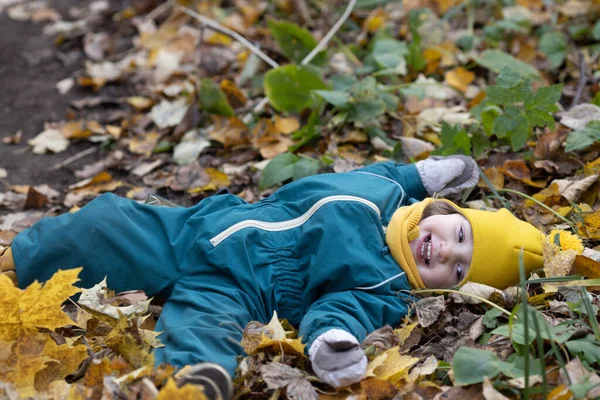Petit enfant couché dans les feuilles d'automne s'amusant dans la forêt — Photo