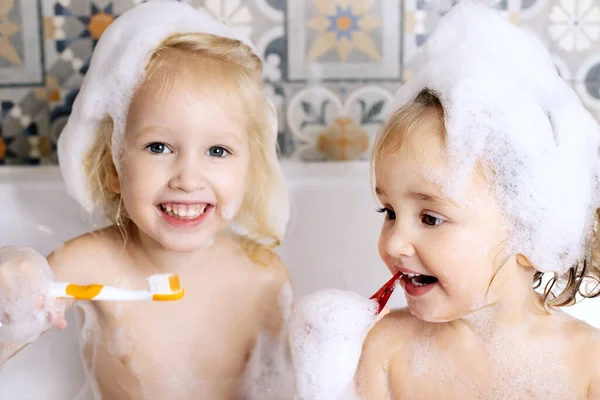 两个清洁牙齿的小女孩坐在浴室里用泡沫洗澡.孩子的个人照顾。家庭快乐 — 图库照片