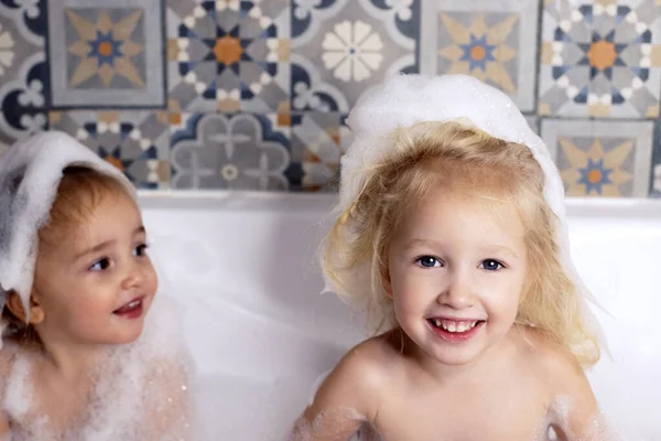 Δύο μικρά κοριτσάκια αδελφές διασκεδάζουν στο μπάνιο παίζοντας με αφρό μπάνιου. Προσωπική φροντίδα παιδιών — Φωτογραφία Αρχείου