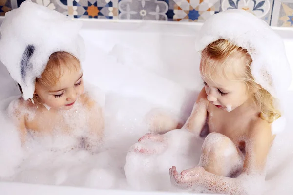 Duas crianças meninas irmãs se divertindo no banheiro brincando com espuma de banho. Crianças cuidados pessoais — Fotografia de Stock