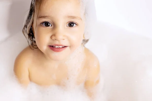 可爱的孩子，长着一双漂亮的大眼睛，坐在浴室里用泡沫洗澡。婴儿护理，个人护理。女孩 — 图库照片