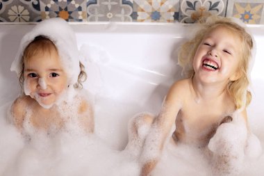 İki küçük kız kardeş banyoda banyo köpüğüyle oynarken eğleniyorlar. Çocuklar kişisel bakım