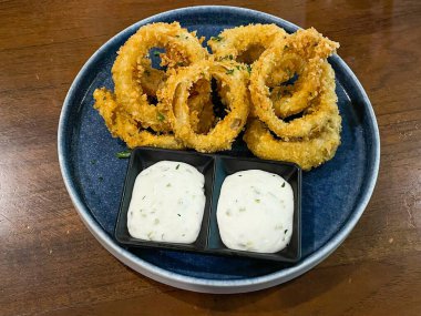 Tahta masadaki tabaktaki sosla birlikte kızarmış soğan halkası.