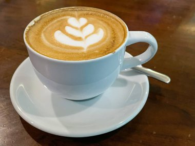 Bir fincan sıcak kahve kapuçino latte sanat seramik bir demlikte ahşap arka planda.