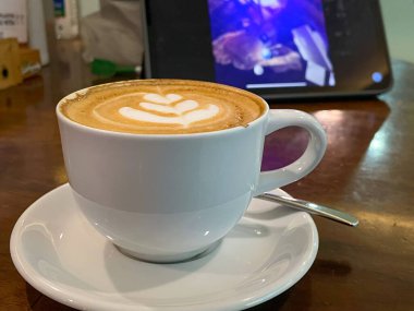 Beyaz fincanda bir fincan sıcak kapuçino ve ahşap masa üzerinde latte sanatı.