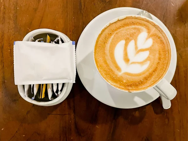 Düz bir fincan kapuçino, beyaz bardakta ve ahşap masada latte sanatıyla.