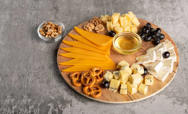 Assorted cheese on a wooden plate on a gray background — Stock Photo, Image