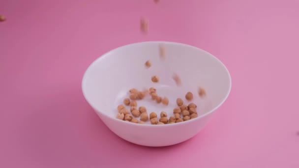 Rohe Kichererbsen werden in eine Schüssel auf rosa Hintergrund gegossen — Stockvideo