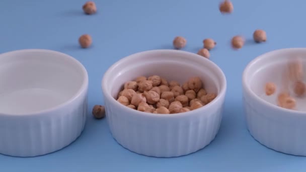 Pois chiches crus tombant dans des assiettes blanches sur fond bleu — Video