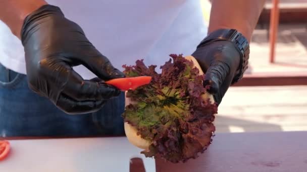 Der Koch legt Tomaten und eine Grillwurst in ein Hot-Dog-Brötchen — Stockvideo