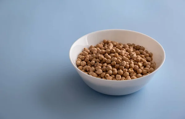 Grains of raw chickpeas in a white bowl on a blue background Stock Image