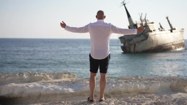 Ampia ripresa di uomo caucasico allungando le mani godendo di leggera brezza dal mare sotto il sole. Vista posteriore di ragazzo libero fiducioso in piedi sulla costa rocciosa ammirando la bellezza della natura all'aperto. Concetto di libertà. — Video Stock