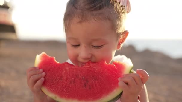 Närbild porträtt av charmig söt liten flicka njuter av smaken av hälsosam vattenmelon på familj picknick utomhus i solsken. Söt glad kaukasiska barn äter frukt på Medelhavet stranden. — Stockvideo