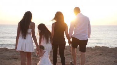 Akdeniz 'de gün batımına kadar yavaş çekimde yürüyen çok nesilli bir ailenin arka görüntüsü. Dertsiz, mutlu, Kafkasyalı baba, anne ve kızları güneş ışığıyla dışarıda geziniyor, gülümsüyor..