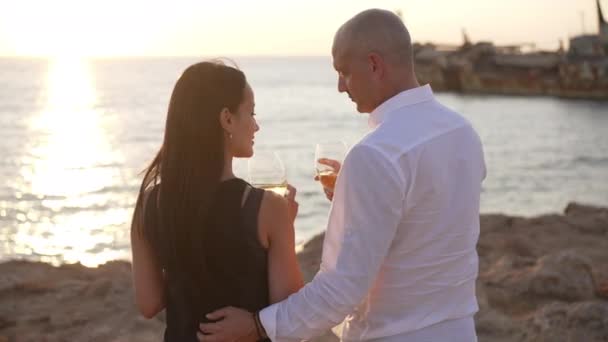 Fecha romántica de pareja caucásica adulta al atardecer en la orilla del mar Mediterráneo. Vista posterior de hombre y mujer cariñosos tintineo tostadas beber vino admirando la belleza de la naturaleza al aire libre. Movimiento lento. — Vídeo de stock