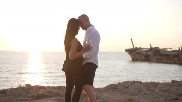 Pareja cariñosa bailando en cámara lenta bajo los rayos del sol al atardecer del mar Mediterráneo. Vista lateral amplia toma de hombre y mujer caucásicos felices disfrutando de la vinculación al aire libre. Concepto romántico de citas. — Vídeos de Stock