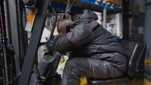 Vista laterale esausto sovraccarico caucasico operatore caricatore magazzino dormire seduto in carrello elevatore. Stanco uomo sovraccarico addormentarsi facendo un pisolino nel sito di stoccaggio industriale. Sovraccarico. Rallentatore — Video Stock