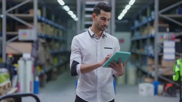 Concentrato barbuto mediorientale agente di trasporto lista di controllo delle spedizioni su tablet in piedi in magazzino industriale guardando intorno a magazzino su rack. Professionale uomo esperto che lavora in magazzino — Video Stock