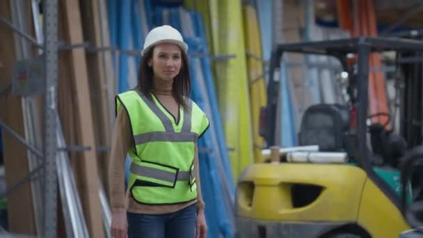 Live-Kamera begleitet junge schöne Frau beim Verlassen der Lagerhalle. Professionelle selbstbewusste kaukasische Mitarbeiterinnen, die lächelnd am Arbeitsplatz in Industrielagern in Innenräumen spazieren gehen. — Stockvideo