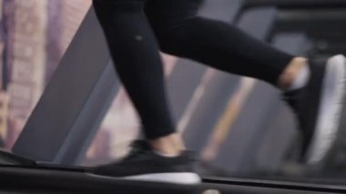 Koşu bandında koşan zayıf genç bir kadının yan görünüşü. Spor ayakkabıları ve spor kıyafetleriyle spor salonunda spor salonunda koşan kendine güvenen bir sporcu. Spor ve spor konsepti.