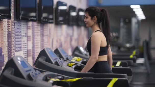 Πλευρική άποψη του χαμογελαστού ταιριάζει Μέση Ανατολή νεαρή γυναίκα με τα πόδια στο διάδρομο στο γυμναστήριο. Πορτρέτο της εμπιστοσύνης λεπτή όμορφη αθλήτρια προθέρμανση προπόνηση σε εσωτερικούς χώρους. Γυμναστική και υγιεινό τρόπο ζωής. — Αρχείο Βίντεο
