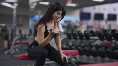 Orta Doğulu kadın vücut geliştirici halter egzersizi yapıyor. Alnını temizliyor. Spor salonunda oturuyor. Kendine güvenen güçlü bir kadının portresi halteri kaldırıyor. Vücut geliştirme ve spor konsepti.