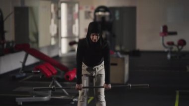 Motive olmuş, tesettürlü, spor salonunda halterle öne eğilmiş bir kadının portresi. Kendine güvenen Ortadoğulu sporcu kadın içeride ekipmanla egzersiz yapıyor. Sağlıklı yaşam tarzı.
