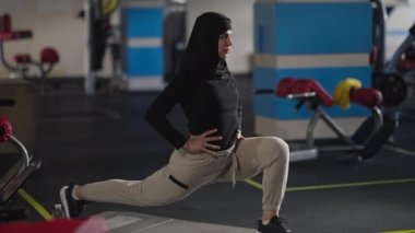 Geniş açılı dayanıklı, tesettürlü sporcu kadın spor salonunda hamleler yapıyor. Ciddi ortadoğulu kadın bacak kaslarını çalıştırıyor. Spor ve spor konsepti.