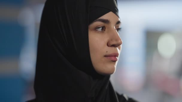 Potret wajah wanita Timur Tengah yang menawan dan percaya diri dalam jilbab hitam yang berpose di dalam ruangan. Wanita cantik langsing yang cantik berpaling menatap kamera dengan ekspresi wajah yang serius. Femininitas dan keindahan — Stok Video