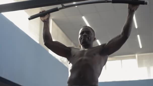 Αφρο-Αμερικανός αθλητής κάνει pull-ups με το φως του ήλιου λάμπει στο μυϊκό σώμα. Μέτριο πλάνο ενός ισχυρού άντρα χωρίς πουκάμισο που κρέμεται στο μπαρ και ξεκουράζεται. Ζωντανή κάμερα κινείται γύρω. — Αρχείο Βίντεο