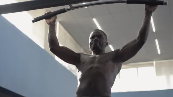 Sportif afro-américain faisant des pull-ups avec la lumière du soleil brille sur le corps musculaire. Plan moyen d'un homme torse nu et motivé, suspendu à la barre et reposant. Caméra en direct se déplace. — Video