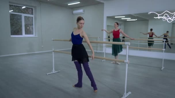 Štíhlá mladá žena nacvičuje taneční sál v baru s baletkou pohybující se v pozadí. Široký záběr koncentrovaných bělošek v místech uvnitř. Umění a koncept zkoušky. — Stock video