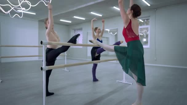 Anmutige schlanke Frauen, die sich mit nach vorne gebeugten Beinen auf tanzenden Barren strecken. Weitschuss schlanke kaukasische konzentrierte Ballerinen, die die Muskeln aufwärmen. Balletttänzer proben im Tanzstudio. Live-Kamera. — Stockvideo