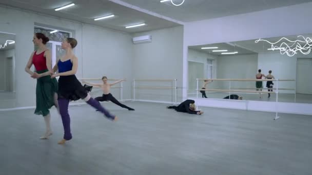 Două balerine subțiri agile repetând pași simultani pirouette cu dansatori de balet care se încălzesc în fundal în studioul de dans. Concentrat talentat caucazian femei dansând în interior . — Videoclip de stoc