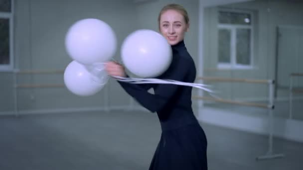 Charming joyful ballet dancer spinning with balloons releasing toys leaving. Portrait of slim gorgeous Caucasian young woman dancing looking at camera having fun rehearsing indoors in studio. — Stock Video