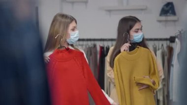 Covid maskeli, kendine güvenen beyaz kadınlar kırmızı ve sarı kazaklarla askılarını değiştirip dükkandan kıyafetlerini seçip, çekip gidiyorlar. Coronavirus 'un güzel müşterileri Kara Cuma.
