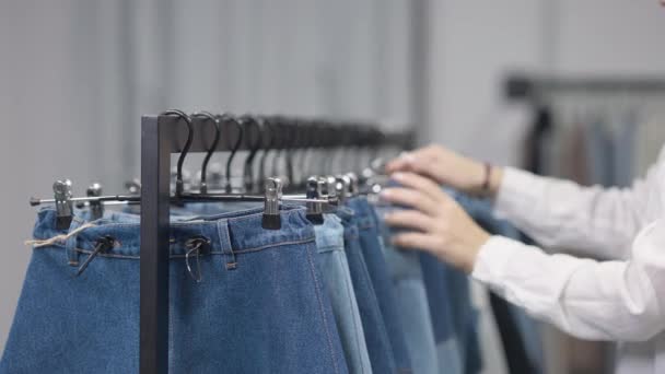 Mulher jovem magro irreconhecível escolhendo roupas jeans na loja em vendas Black Friday. Consumidor caucasiano fêmea tocando cabides em rack pensando examinando vestuário. Consumismo e conceito de desconto. — Vídeo de Stock