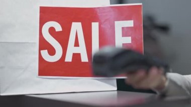 Bulanık beyaz kadın eli ile yapılan satış duyurusu. Akıllı telefondan ve terminalden nakit para alınmıyor. Kara Cuma günü dükkânda tanınmayan satıcı ve alıcı.