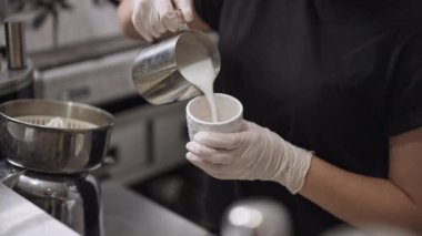 Kahve bardağına sıcak süt döken bir kadın kahve makinesinde ağır çekimde kahve makinesinin başında dikiliyor. Tanınmayan bayan barista nefis taze demlenmiş kapuçino hazırlıyor..
