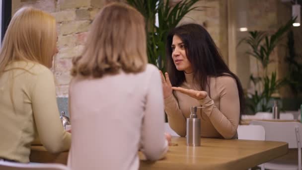 Orta Doğulu güzel, heyecanlı bir kadın kafeterya restoranında oturan beyaz arkadaşlarıyla sohbet ediyor. Gülümseyen, rahat, genç bir bayanın portresi ağır çekimde sohbet ediyor.. — Stok video