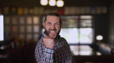 Heyecanlı sakallı mutlu adam zafer jesti yapıyor kameraya bakıp gülümsüyor. İçerde sevinç içinde poz veren heyecanlı beyaz adamın ön manzara portresi. Mutluluk ve heyecan kavramı.